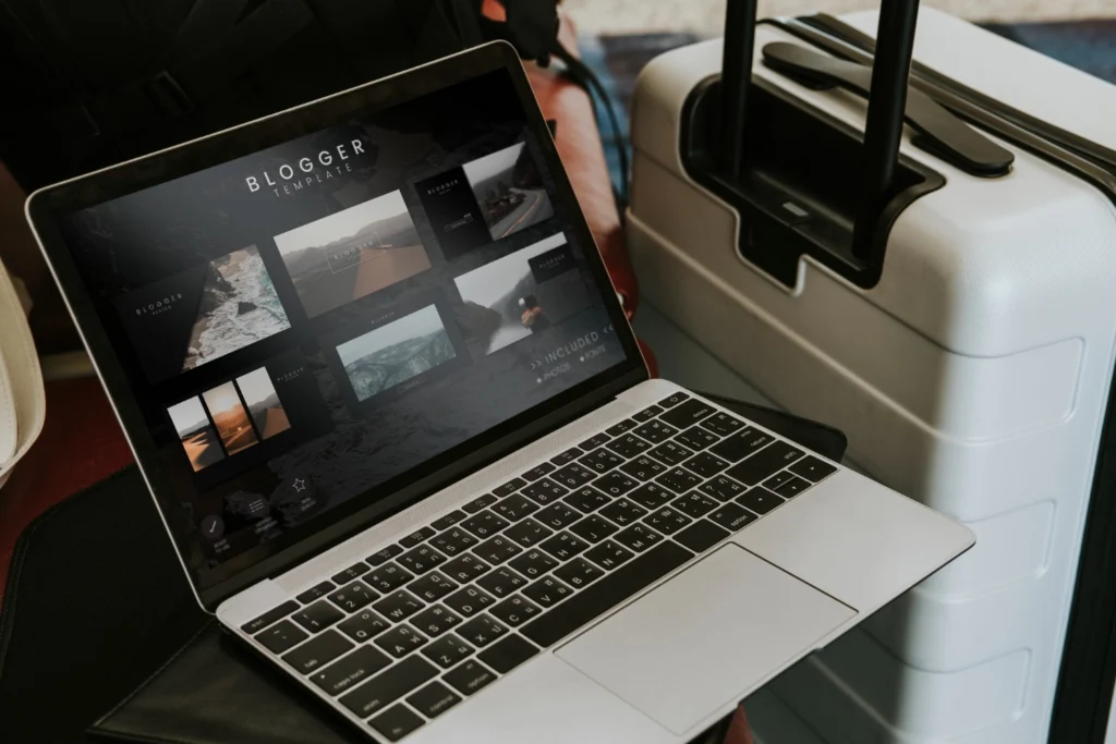 Laptop exibindo blog de viagens ao lado de uma mala no aeroporto.​