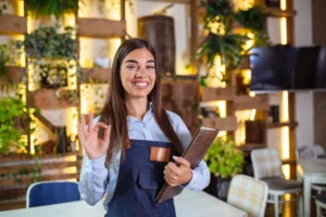 Garçonete sorridente segurando um menu em restaurante, ilustrando um exemplo de serviço com baixo custo para empreender.